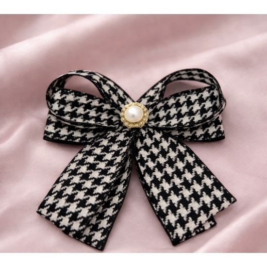 Elegancka broszka w formie kokardy w klasyczny wzór pepitki, wykończona perłowym środkiem – ponadczasowy dodatek do stylowych stylizacji.